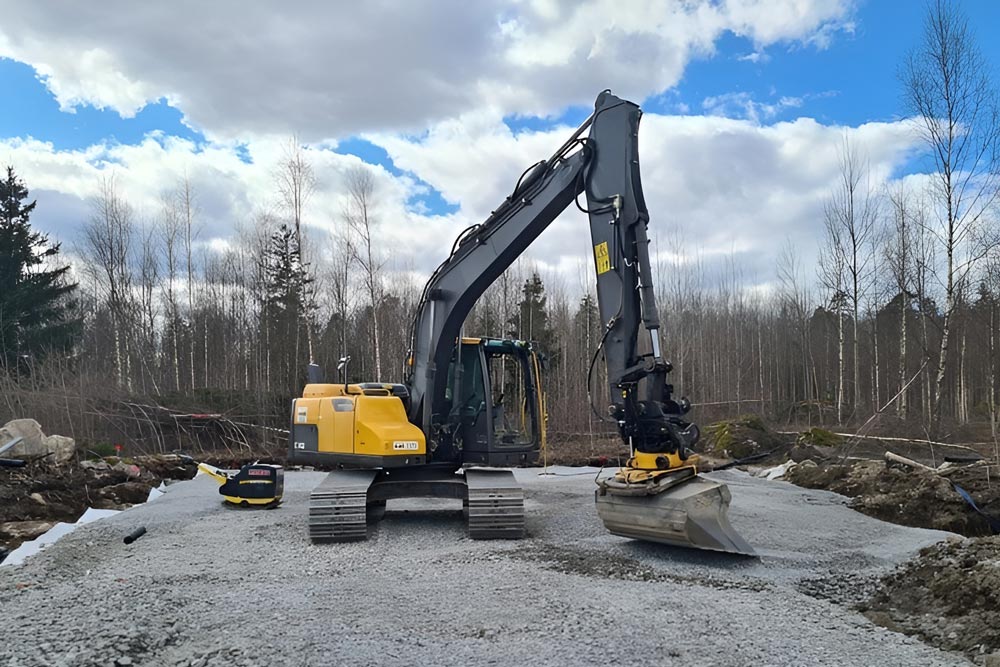 Stor gul grävmaskin med omringande skog