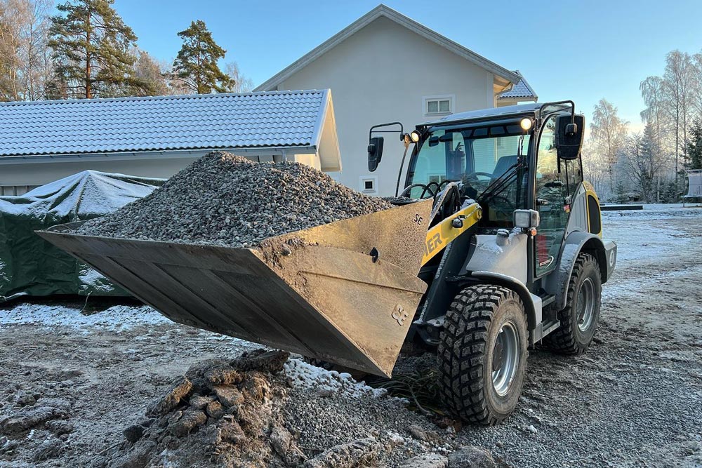 Mindre grävmaskin som bär på grus